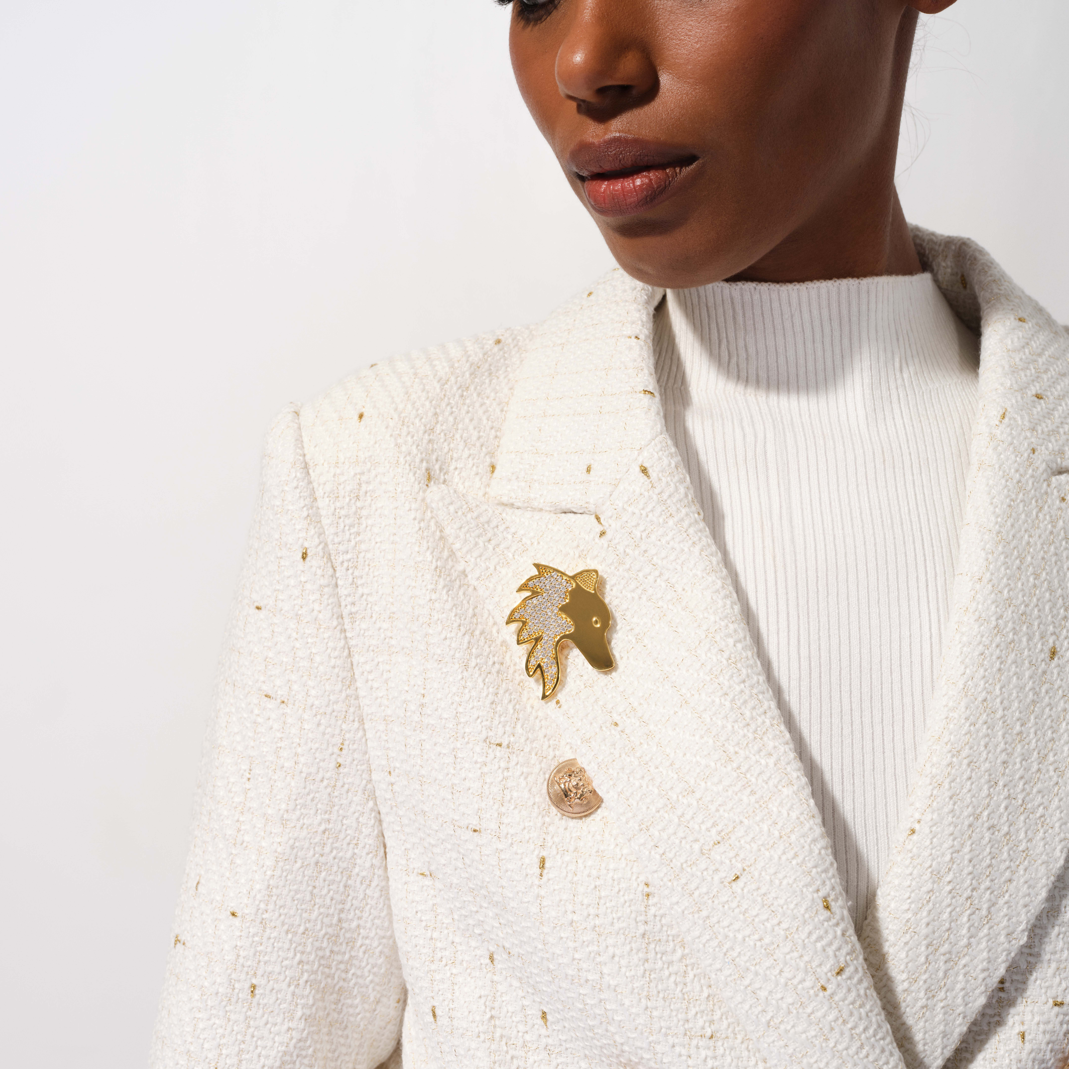 Person wearing a white textured blazer with decorative buttons on a plain background