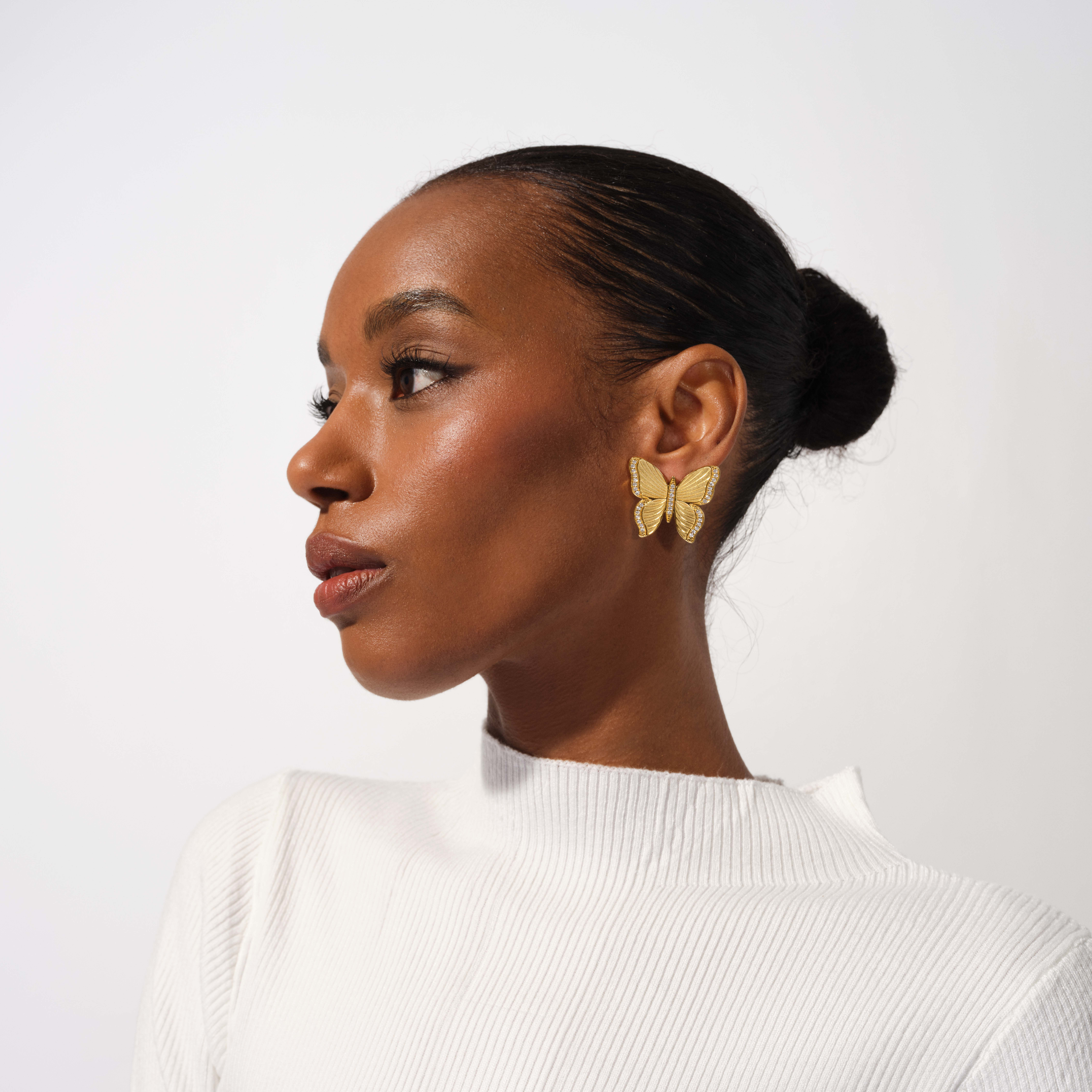 Woman wearing gold butterfly earrings on a white background