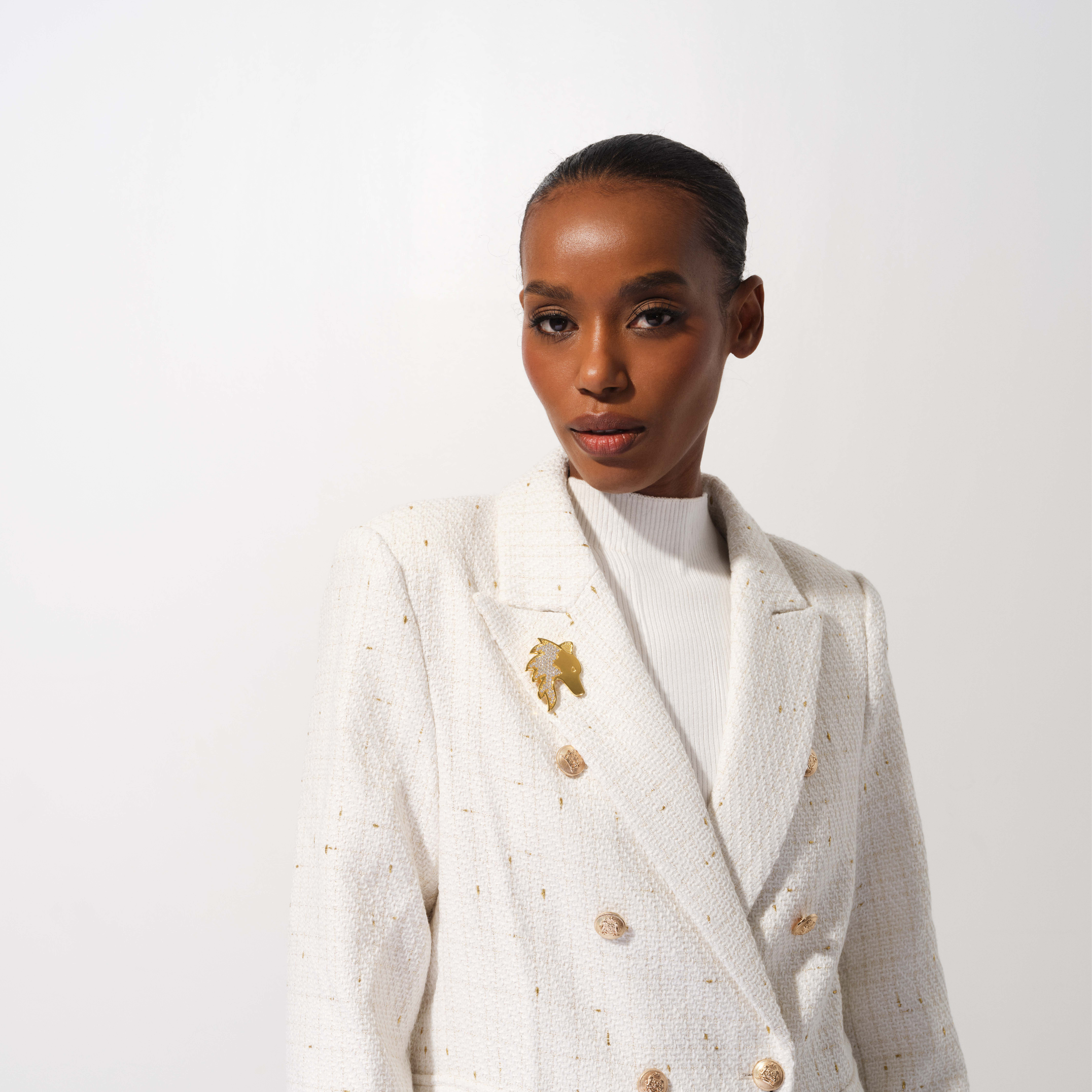 Woman wearing a white blazer with gold buttons and details on a white background