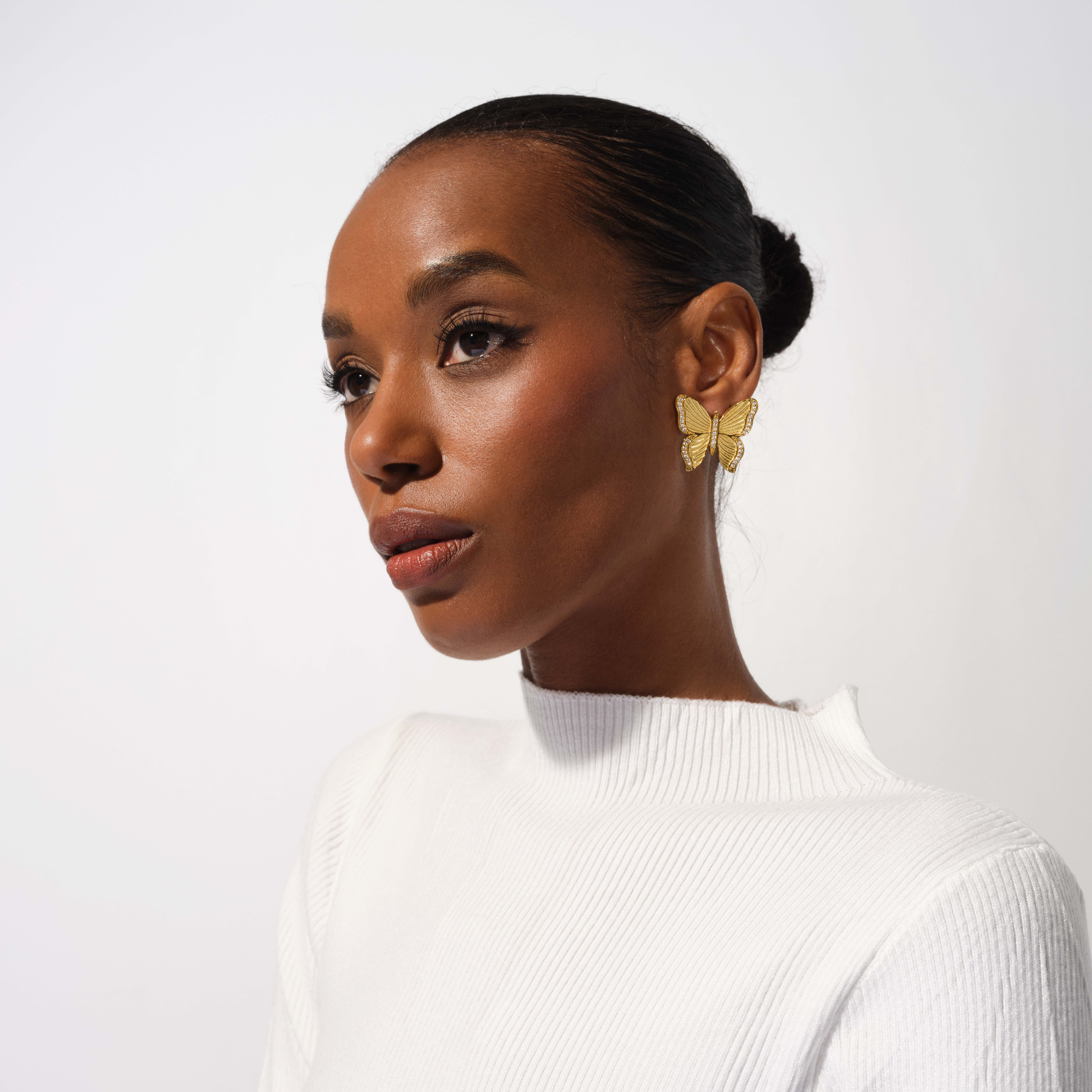 Woman wearing gold butterfly earrings against a white background