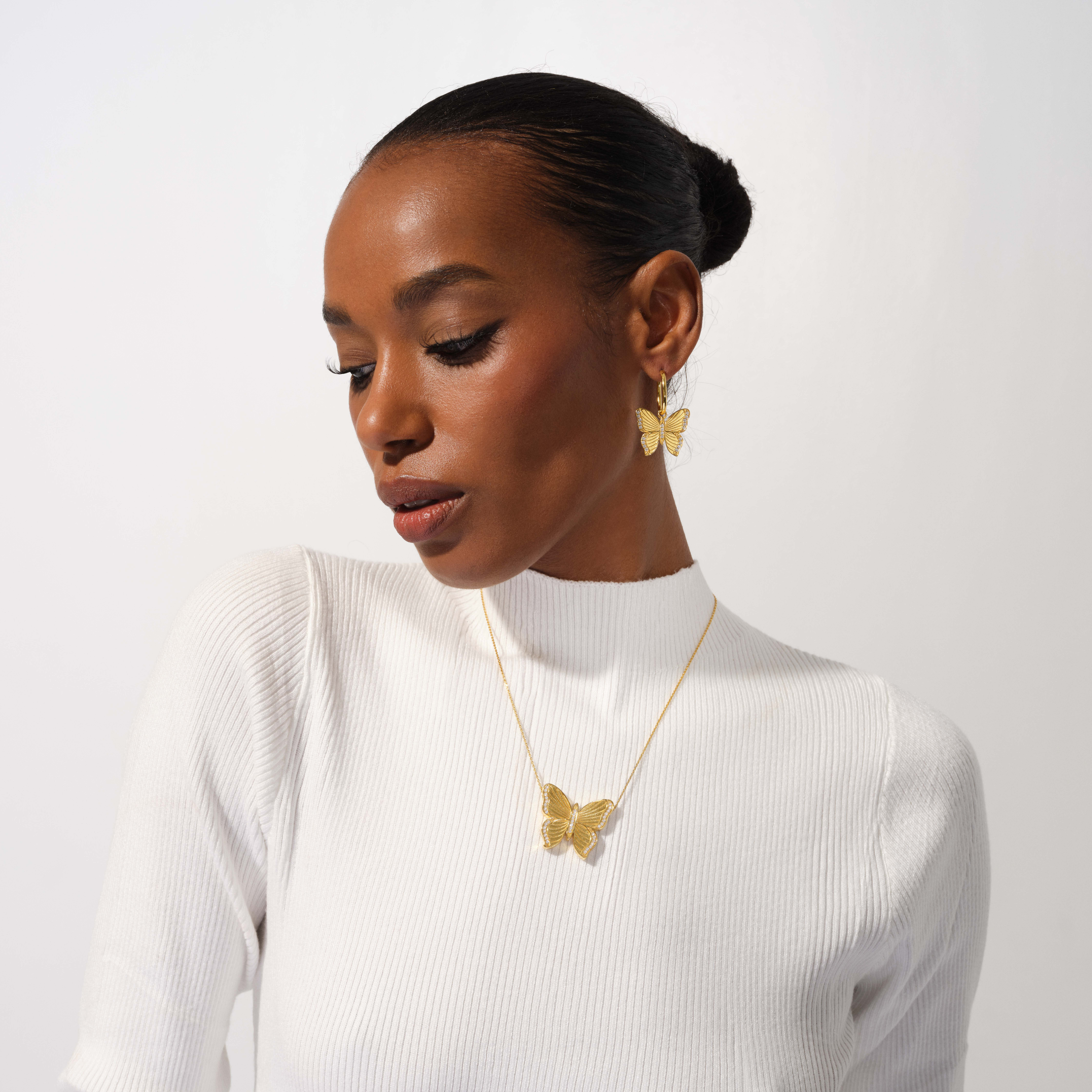 Woman wearing gold butterfly earrings and necklace against a white background