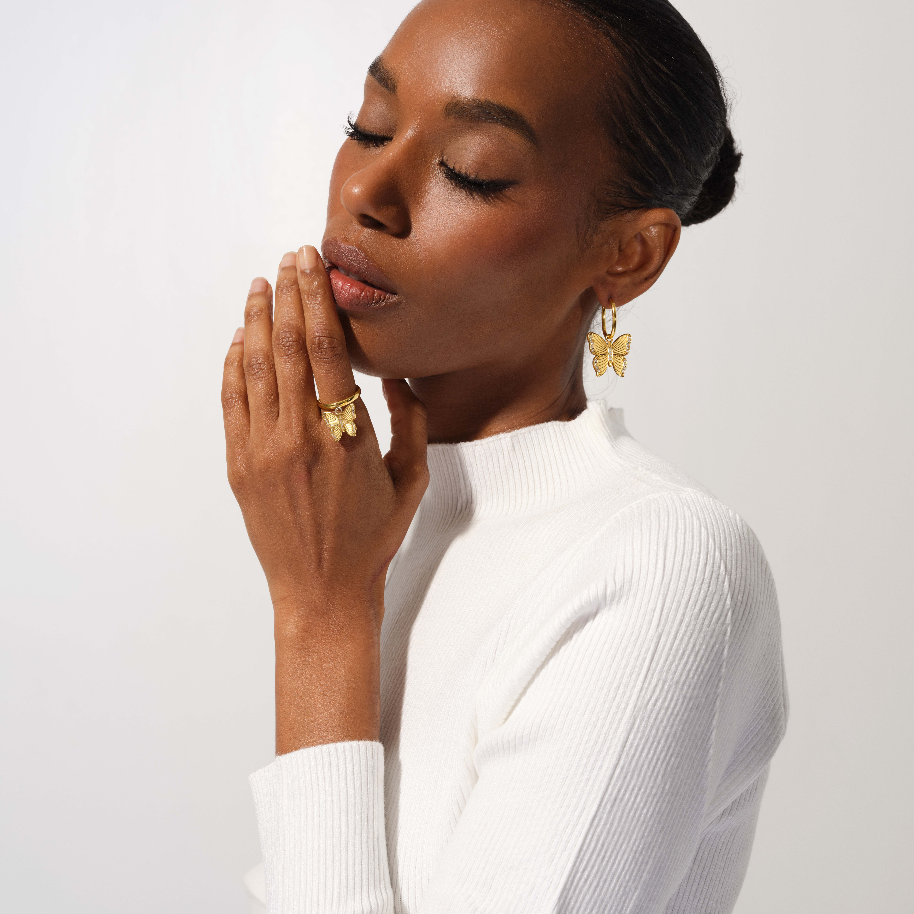 Woman wearing gold butterfly earrings and ring against a white background