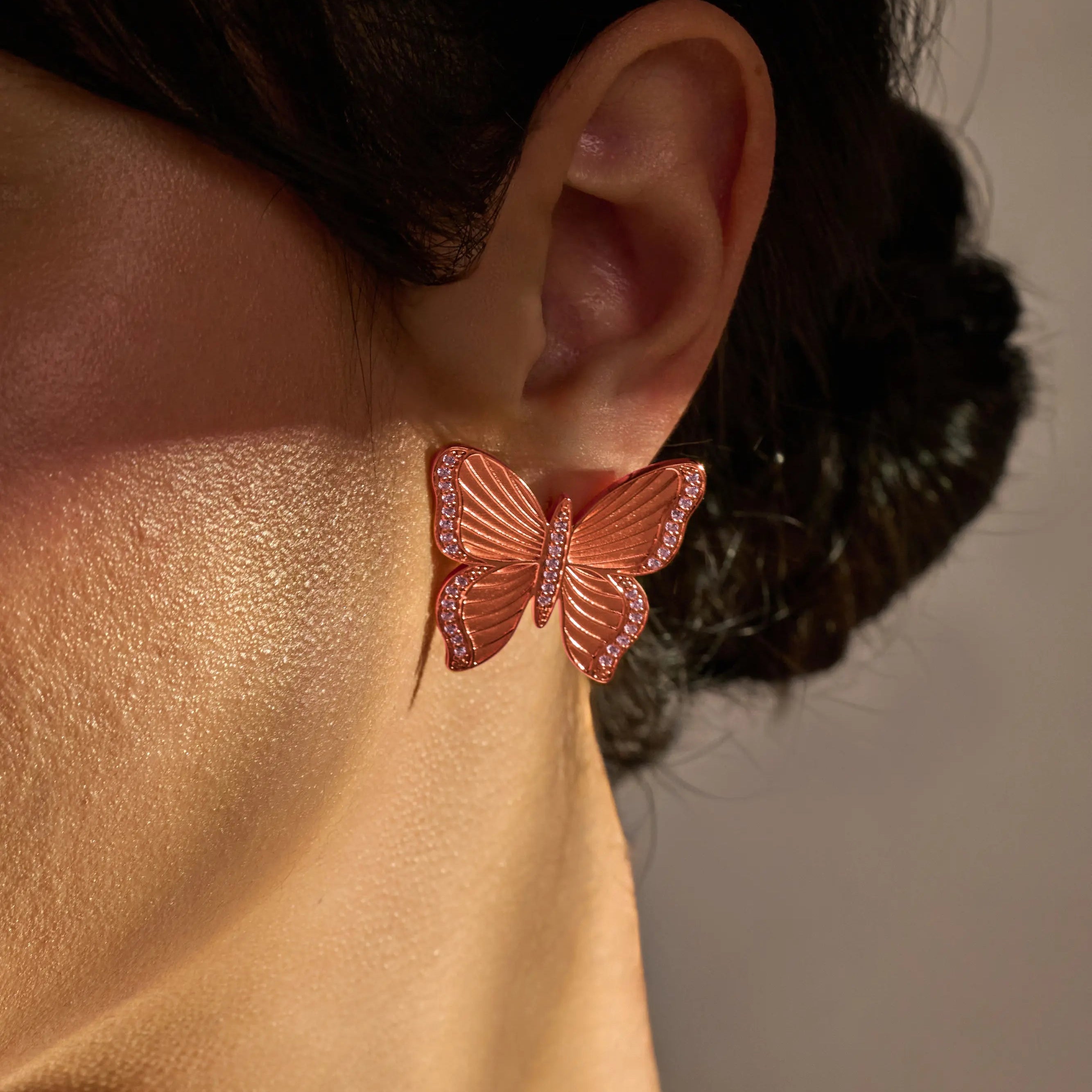 Butterfly-shaped earrings worn by a person with a neutral background