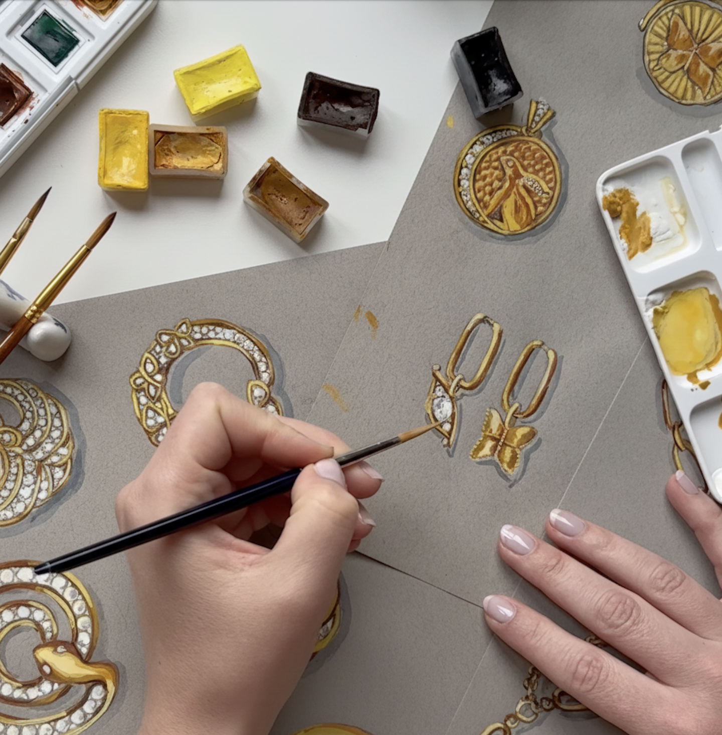 Artistic depiction of gold jewelry designs on paper with paint palette and brushes.