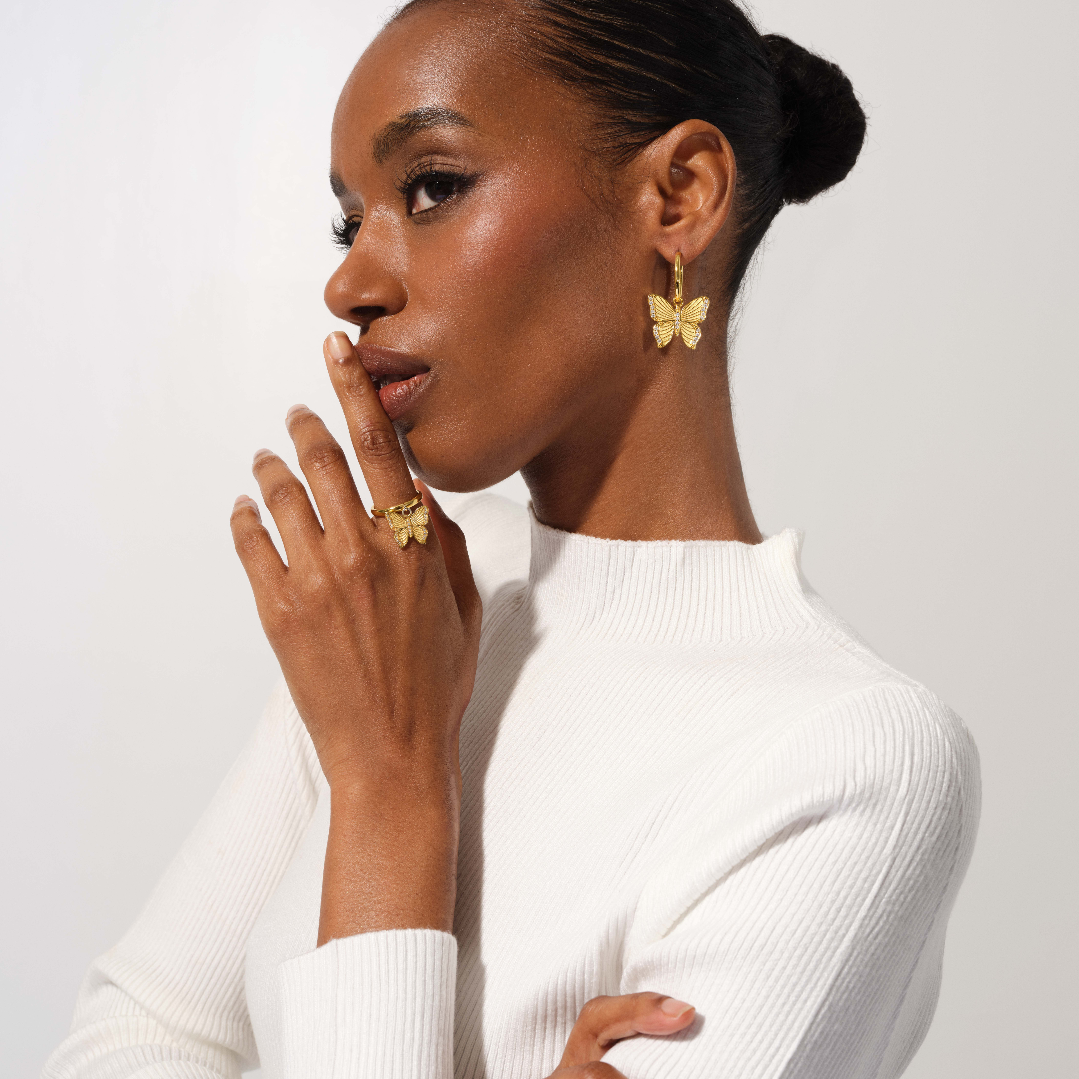 Woman wearing butterfly earrings and ring on a plain background