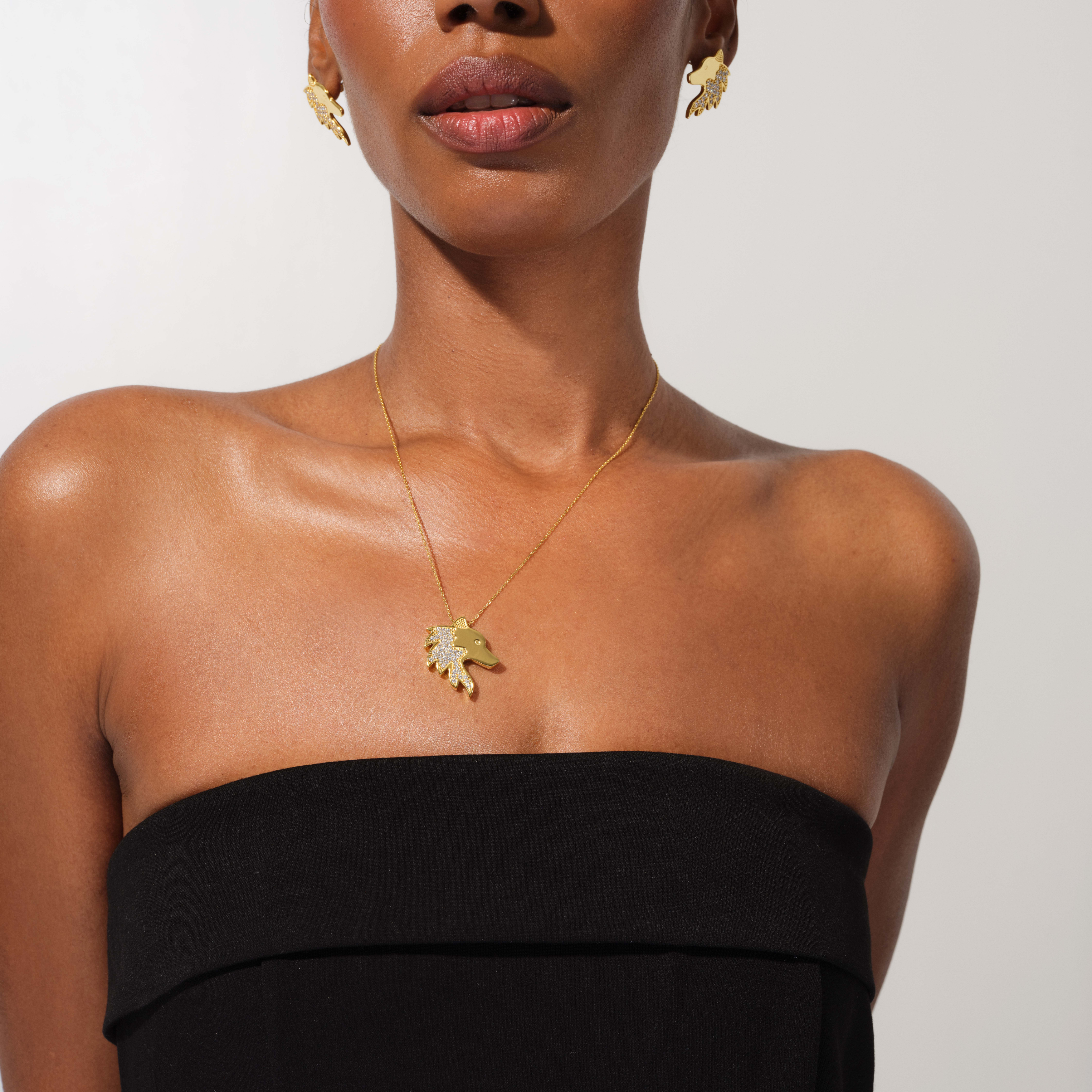 Woman wearing a gold necklace with a leaf pendant on a plain background