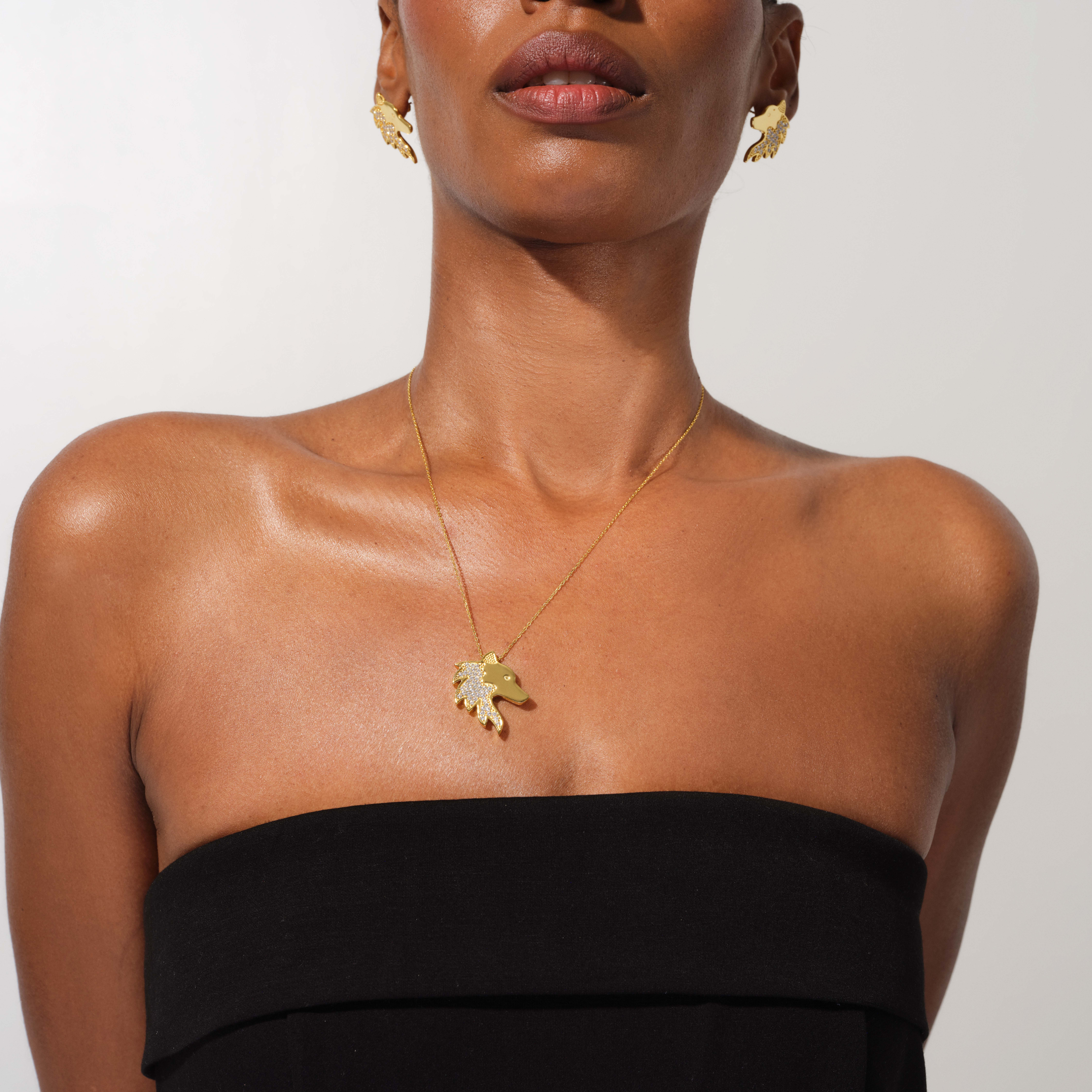 Woman wearing a gold necklace with a leaf pendant on a plain background